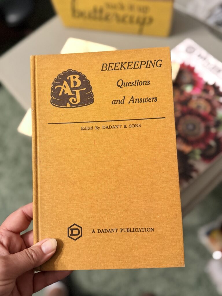 img_0910 › 200 Fingers & Toes Orange beekeeping booklet titled 'Beekeeping Questions and Answers' with the Dadant & Sons logo and 'A Dadant Publication' at the bottom, held in a hand.